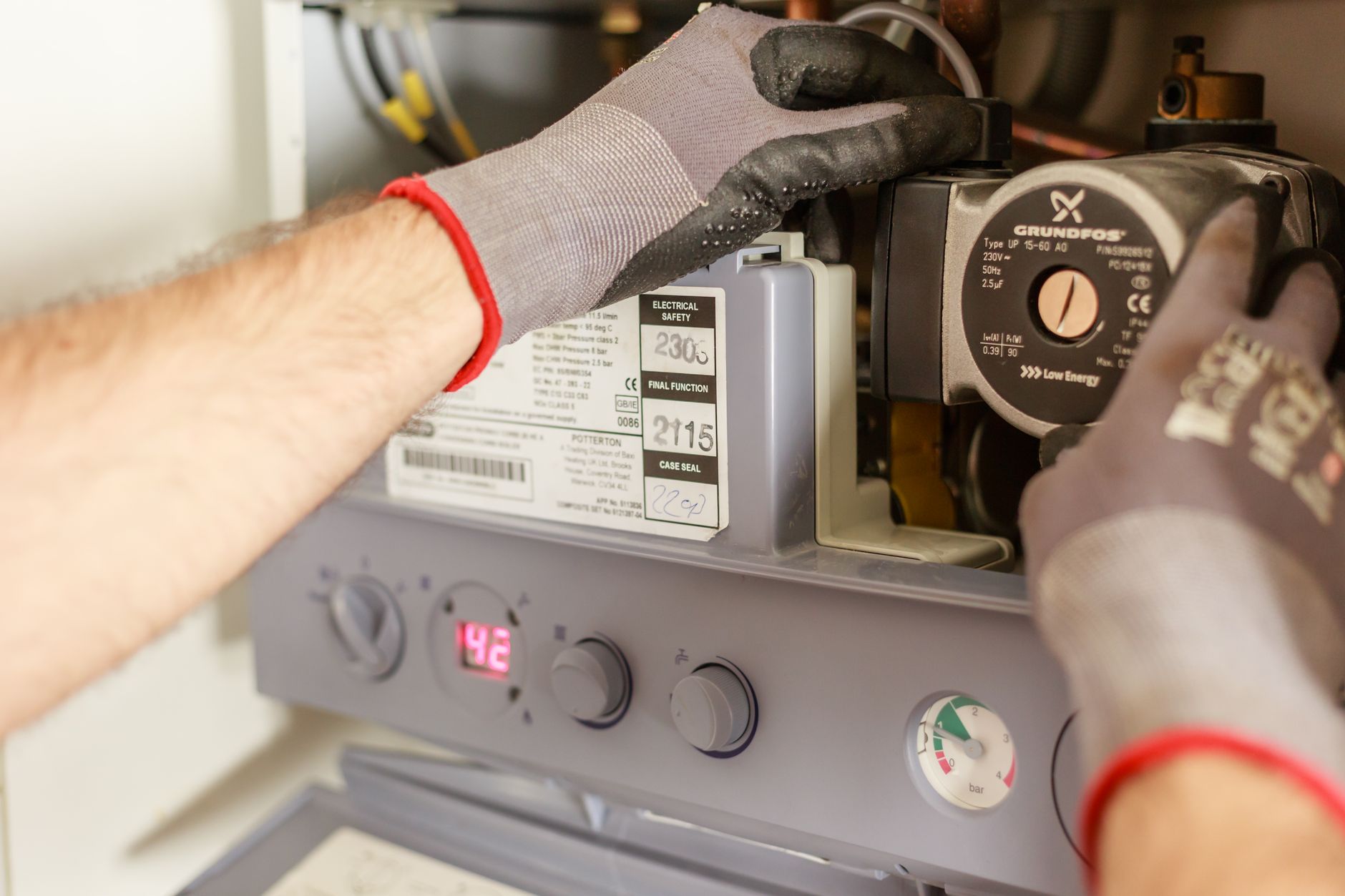 Mains gantées d'un technicien à l'intérieur d'une chaudière murale ouverte