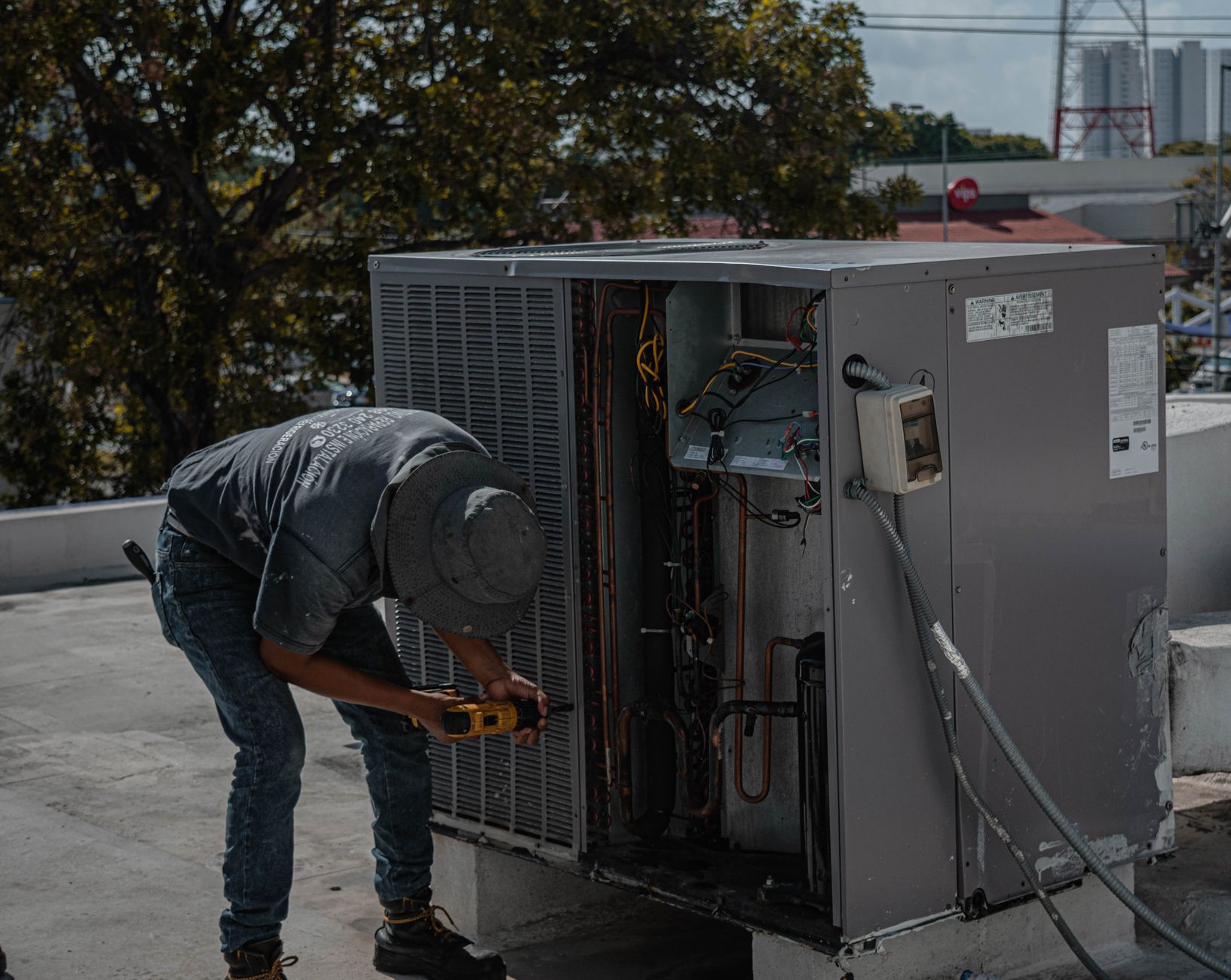 Technicien penché sur un groupe de climatisation en toiture, ses deux mains sur un outil